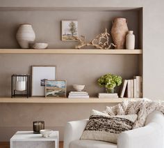 a living room with two white chairs and some books on the shelf above it is a coffee table