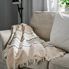 a couch with a blanket on top of it next to a lamp and potted plant