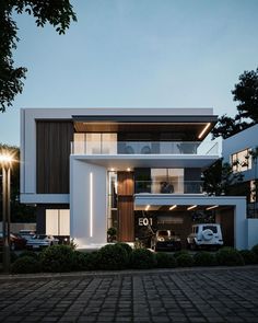 a modern house with two cars parked in the driveway and lights on at night time