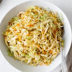 a white bowl filled with coleslaw on top of a table next to a spoon