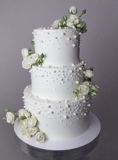 a three tiered wedding cake with white flowers and pearls on the top, sitting on a table