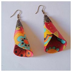 two pairs of colorful fabric earrings hanging from hooks on a white surface, one with an origami design and the other with metal ear wires