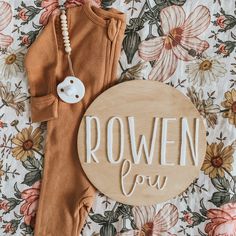 a wooden sign that says rowen you next to a baby's outfit