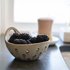 a bowl filled with blackberries sitting on top of a counter next to a cup