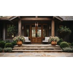 the front entrance of a house with two chairs and flowers in large planters on the steps