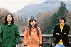 three people standing next to each other in front of trees and mountains with hills in the background