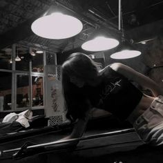 a woman leaning on the edge of a pool table in a room with lights overhead