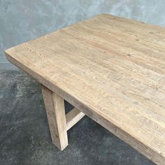 a wooden table sitting on top of a cement floor next to a gray wall in an empty room