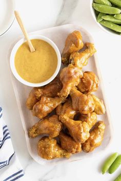 chicken wings on a plate with dipping sauce and green beans next to it in a bowl