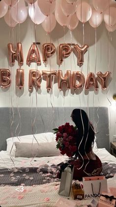 a woman is sitting on her bed with balloons and presents in front of her,