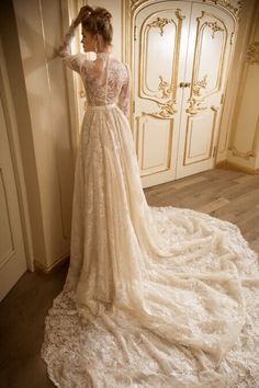 a woman standing in front of a white door wearing a wedding dress with long sleeves