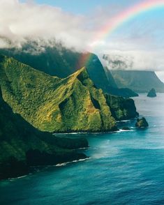 a rainbow shines in the sky over an island with green mountains and blue water