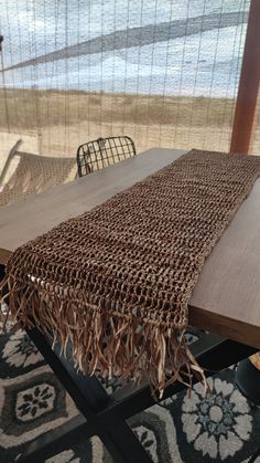 a wooden table with a brown cloth on top of it next to chairs and an ocean view