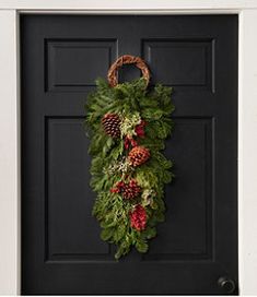 a black door with a wreath and pine cones hanging on it's front door