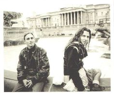 two young men sitting next to each other in front of a large building with columns