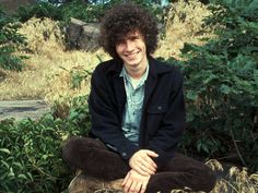 a young man sitting on top of a tree stump in the woods smiling at the camera