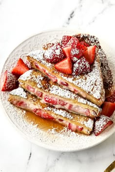 a white plate topped with french toast covered in powdered sugar and sliced strawberries