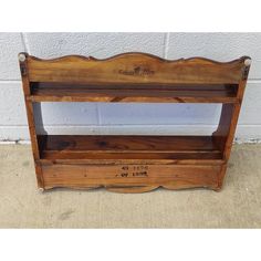 an old wooden shelf with writing on the front and bottom, sitting against a white brick wall