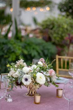 an arrangement of flowers in vases on a pink table cloth at a wedding reception