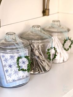 three glass jars with christmas decorations in them on a counter top next to a faucet