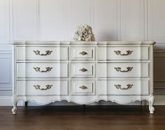 an antique white dresser with gold handles and knobs on the drawers, against a wall