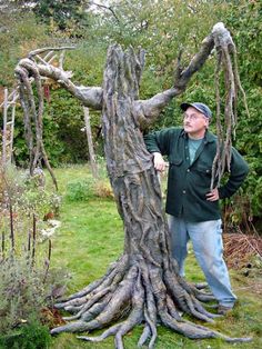 a man is standing next to a tree with roots growing out of it in the grass