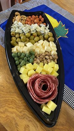 a boat shaped platter filled with different types of cheeses, meats and vegetables