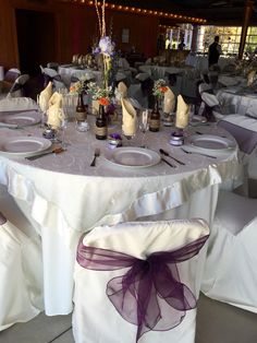 the table is set with white linens and purple ribbons