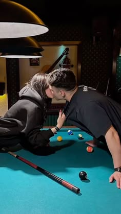 a man and woman playing pool in a dark room with billiards on the floor