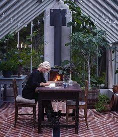 a person sitting at a table with a lit candle in their hand and some potted plants on the other side