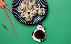 a plate with sushi and chopsticks next to it on a green surface