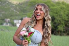 a beautiful young woman holding a bouquet of flowers in her right hand and smiling at the camera