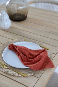 a place setting on a wooden table with an orange napkin and gold fork resting on the plate