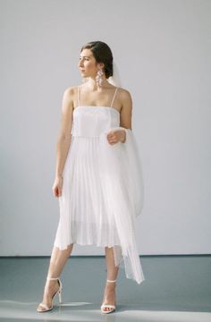 a woman in a white dress and high heels standing on a gray floor with her back to the camera