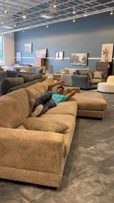 a man laying on top of a large couch in a living room filled with furniture