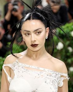 a woman with black hair and makeup on her face wearing a white dress in front of photographers