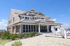 a large house with two lawn chairs in front of it on the sand and grass