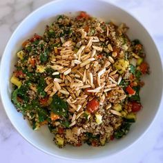 a white bowl filled with lots of food on top of a marble countertop next to a wooden spoon