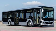 a black and silver bus is parked on the road with its driver in it's seat