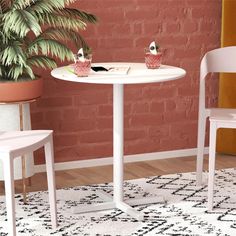 two chairs and a table in front of a brick wall with potted plants on it