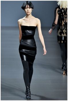 a woman walking down a runway in a black dress