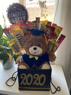 a graduation teddy bear sitting in a box filled with candy and congratulationss for grad