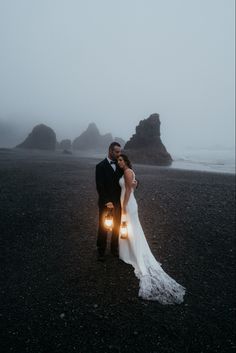 a bride and groom standing on the beach with their lights in front of them