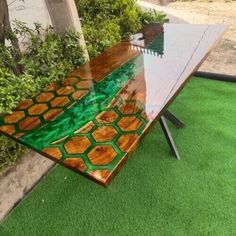 a table made out of wood and glass with green paint on the top, sitting on artificial grass