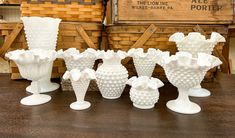 several white vases sitting on top of a wooden table next to baskets and boxes