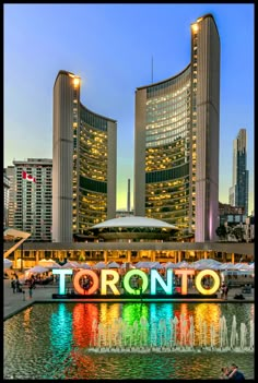 there is a sign that says toronto in front of some tall buildings with lights on them