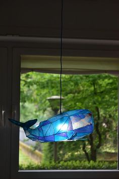 a blue stained glass bird feeder hanging from a window with trees in the back ground