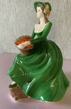 a ceramic figurine with a green dress and hat holding a bowl filled with food