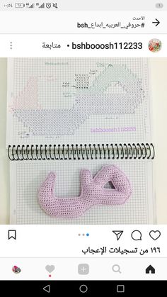 a pink crocheted object sitting on top of a spiral notebook next to a pen