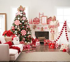 a woman standing in front of a christmas tree with presents on the floor next to it